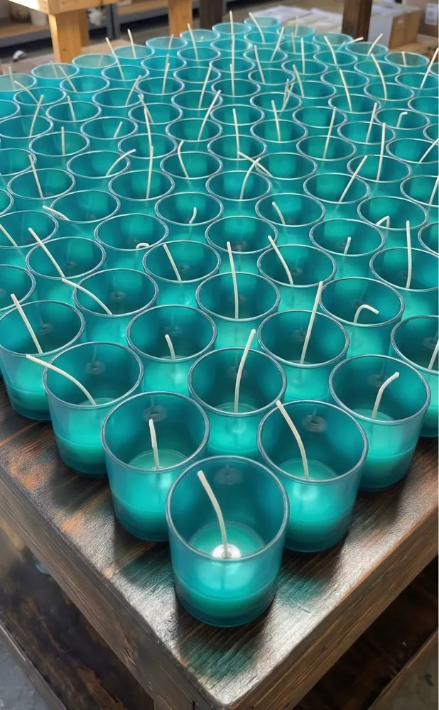 Teal glass candle vessels with wicks in rows on a wooden studio table